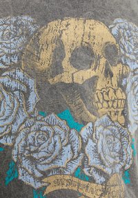 Camiseta gris oscuro con un gráfico de calavera dorada rodeada de rosas azules y acentos en azul verdoso, con una pancarta que dice "Satisfacción."