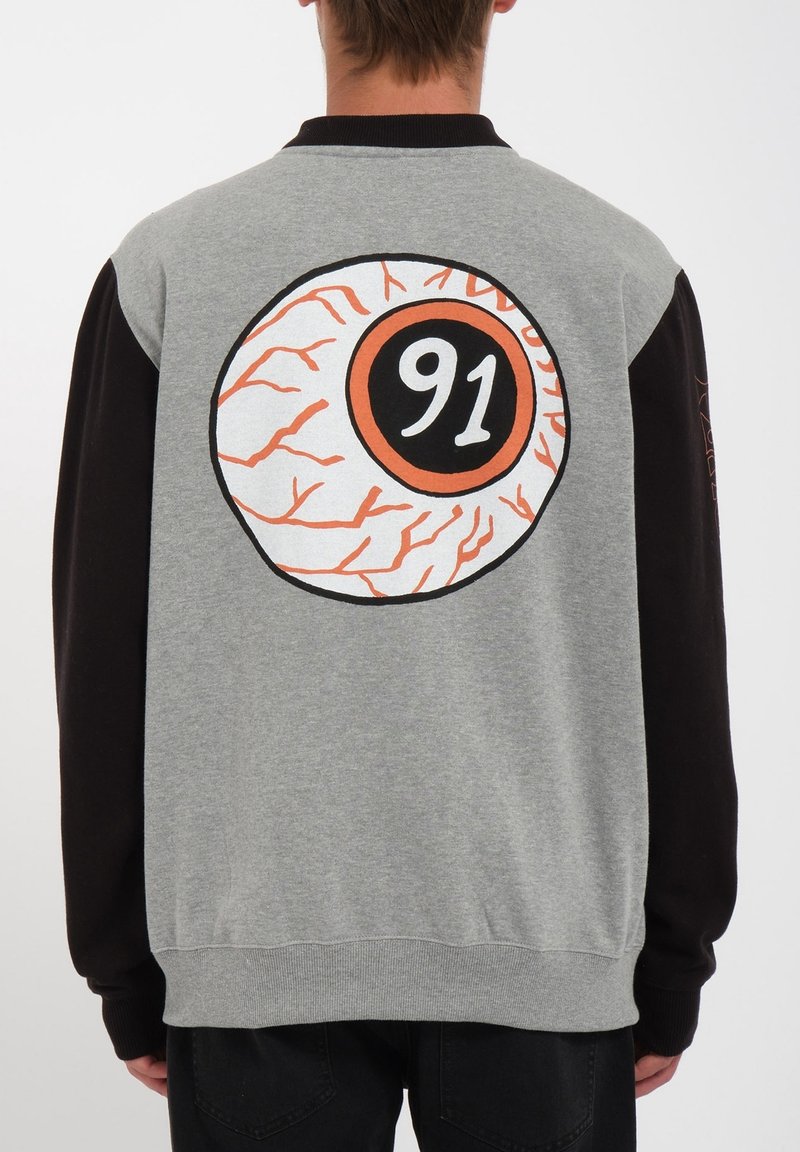 Personne portant une veste grise et noire avec un grand dessin d'œil et le numéro 91 au centre du dos.
