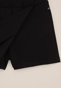 Schwarze, gesteppten Stoffshorts mit Faltendetail und kleinem, aufgenähtem Logo-Tag vor schlichtem Hintergrund.