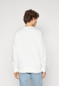 Hvid sweatshirt med lange ærmer og rund halsudskæring. Har en glat tekstur samt ribbede manchetter og kant, båret med lyseblå jeans.