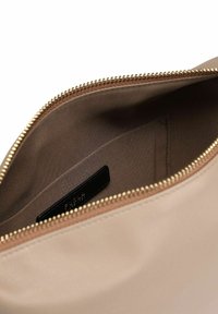 Pochette en cuir beige avec une fermeture éclair dorée. L'intérieur est doublé d'un tissu marron lisse et comporte une petite étiquette noire. Design simple et minimaliste.