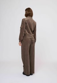 Barna kordbársony zakó- és nadrágszett, bordázott textúrával, kényelmes szabással és széles szárakkal, oldalzsebekkel és elasztikus mandzsettákkal.