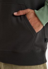 Sudadera gris oscuro con un bolsillo canguro, dobladillo acanalado y puños en un verde claro contrastante. Material suave con textura lisa.