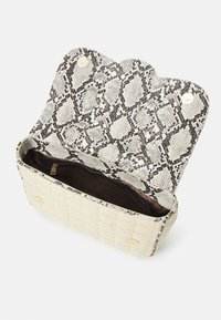 Beige kankainen ja käärmeennahkakuosiset käsilaukku, jossa on aaltoileva läppä, kultaiset yksityiskohdat ja sisäinen vetoketjullinen tasku.