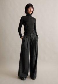 Zwarte coltrui met een subtiele glans, gecombineerd met hooggewaisted, wijde grijze broek met voorplooien en zijzakken.