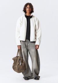 Chaqueta de forro polar blanca con cremallera, camiseta negra, jeans de pierna ancha grises y un bolso marrón. Presenta herrajes plateados y un material texturizado.