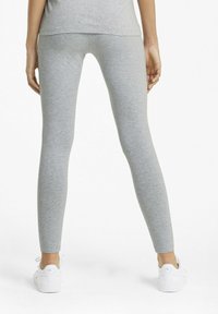 Szürke leggings rugalmas anyagból, testhezálló kivitel, bokáig érő hossz, fehér sportcipővel párosítva. Sima textúra, minimalista stílus.