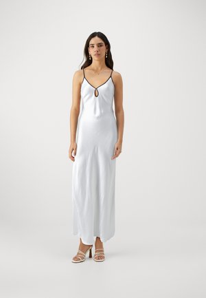 White satin maxi dress with black trim, featuring a keyhole detail at the neckline. Model wears strappy beige heels. Smooth texture.