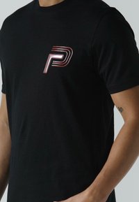 Melna kokvilnas T-krekls ar spīdīgu sarkano un baltu "P" logotipu kreisajā krūtī. Īsas piedurknes un klasiskā apaļā apkakle.