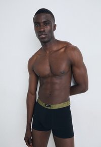 Svart boxer短sy med et grønt mønstrete liv. Glatt stoff, tettsittende design, og ingen synlige logoer bortsett fra en liten etikett på livet.