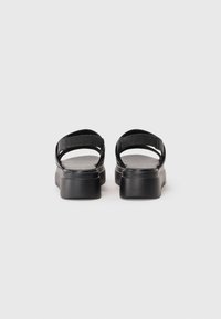 Svarte sandaler med bred remdesign, glatt tekstur og en kraftig såle med lett heving. Justerbare ankelremmer inkludert.