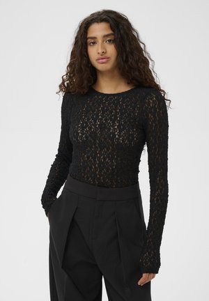 Top nero a maniche lunghe realizzato in pizzo texturizzato, con scollatura rotonda e design aderente, abbinato a pantaloni larghi neri.