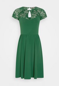 Zielona sukienka z koronkowymi rękawami w kształcie kaptura, dekoltem w kształcie łezki i rozkloszowanym dołem. Wykonana z miękkiego, elastycznego materiału o gładkiej fakturze.