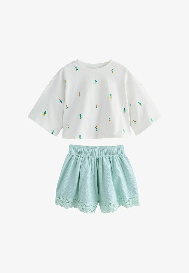 Camiseta blanca recortada con pequeños estampados de flores coloridas combinada con pantalones cortos azul claro de cintura elástica con ribete de encaje con borde festoneado.