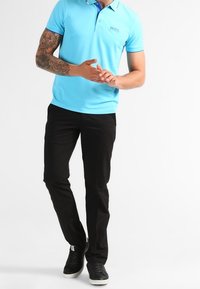 Ljusblå pikétröja med krage och logotyp, kombinerad med svarta slim fit-byxor och svarta sneakers. Slät textur, avslappnad design.