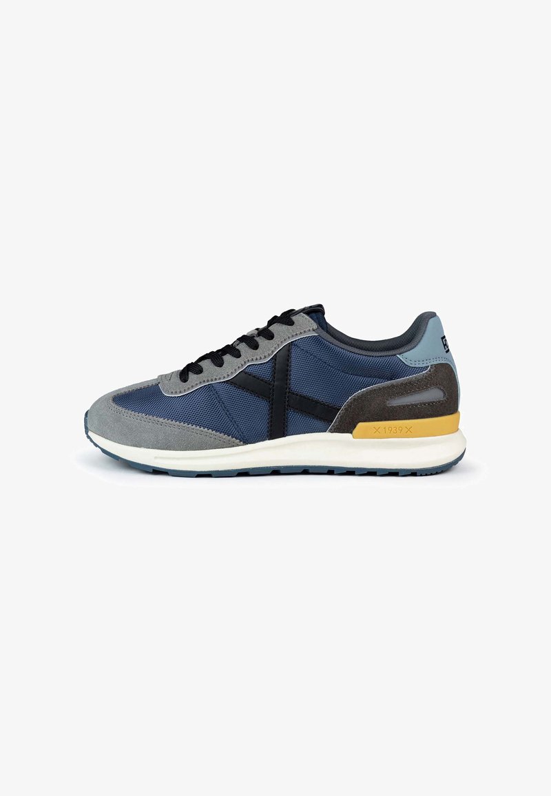 Navy and gray sneaker featuring a mesh upper, suede accents, black laces, and a yellow heel detail on a white midsole with a textured outsole.