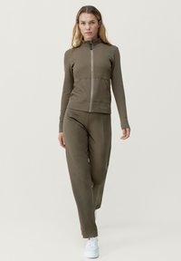 Felpa con zip verde oliva e pantaloni abbinati in tessuto a costine. Presenta un colletto alto, tasche laterali e calzature bianche.