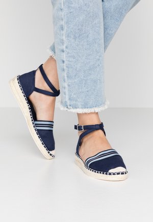 Navy espadrille shoes with striped fabric upper, ankle strap, and woven jute sole. Rounded toe with contrasting stitching details.