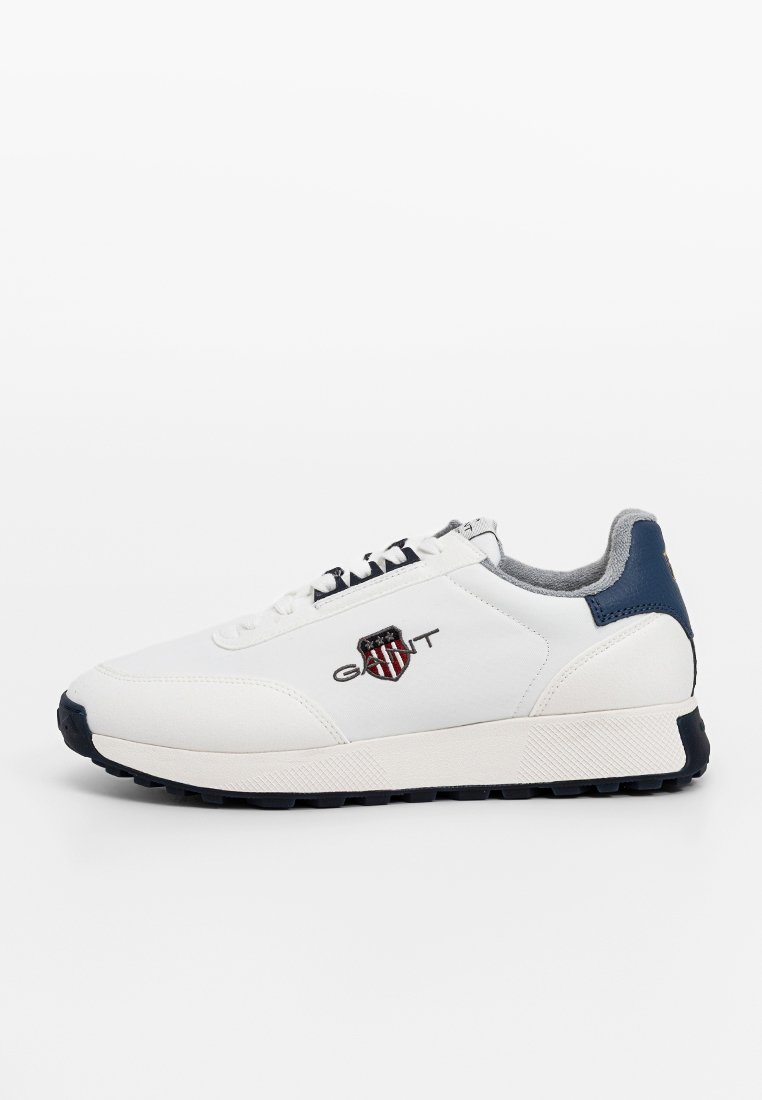 Sneaker bianca con accenti blu navy, tomaia in pelle e tessuto, punta rotonda, suola piatta e logo ricamato. Presenta dettagli testurizzati sulla suola.