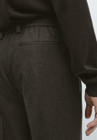 Person wearing dark gray tailored pants and a black ribbed long-sleeve sweater, with hand relaxed at side.