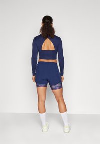 Crop top de manga larga azul marino con un corte en la espalda, combinado con pantalones cortos azul marino con un dobladillo estampado multicolor. El conjunto se completa con calcetines y zapatos blancos.