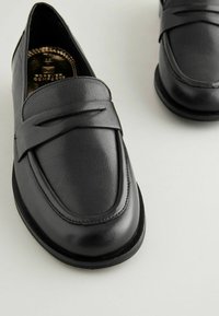 Sorte læder loafers med en glat tekstur, der har et stilfuldt bånd over vristen og en rund tå. Blød sål for komfort.