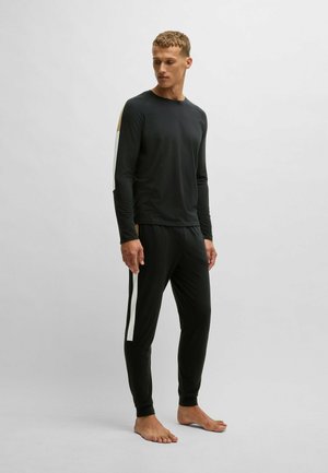 Zwart langemouwen shirt en broekset. Het shirt heeft gouden en witte accenten op de mouwen. Gladde stof, slim fit, elastische tailleband op de broek.