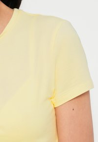 Keltainen lyhythihainen t-paita, jossa on sileä pinta ja klassinen istuvuus. Siinä on yksinkertainen pääntie ja kevyesti ommellut reunat.