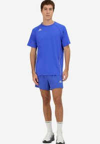 T-shirt e pantaloni corti sportivi blu realizzati in tessuto leggero. Presentano un collo a giro, maniche corte e accenti del logo sul petto e sulla gamba.
