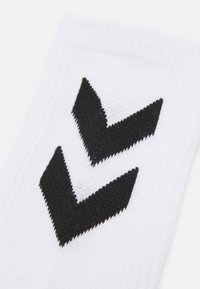Fehér zoknik, két fekete chevron mintával. Az anyag texturált kötésű, a tetején bordás széllel.