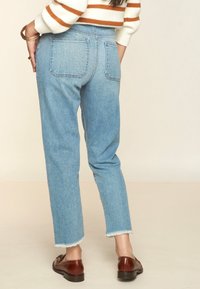 Helles blauer Denim-Jeans mit hoher Taille, geradem Bein und fransigem Saum. Verfügt über zwei Gesäßtaschen und sichtbare Nähte.