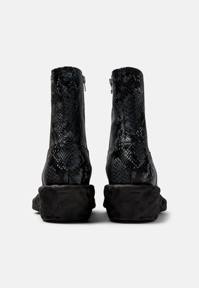 Svarta ankelboots med ett texturerat ormskinnsmönster, sidogärningar och en kraftig, skulpturerad svart gummisula.