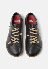 Svarta läderskor med beige snören, med en texturerad yta och gummisula. Inuti finns röda innersulor märkta "CAMPER TWINS."