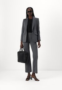 Gray tailored suit with a fitted blazer and matching pants, paired with a black blouse. Accessories include a sleek black handbag and sunglasses.
