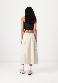 Beige cargo skirt with side pockets, high waist, and flowing silhouette. Paired with a black crop top and light pink sneakers.