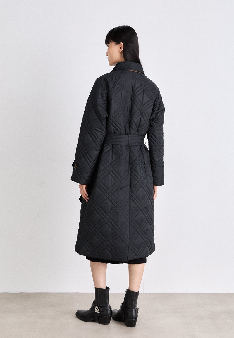 Cappotto nero imbottito con vita cinturata, caratterizzato da un motivo a rombi e maniche lunghe. Abbinato a stivaletti, indossato sopra un outfit nero.