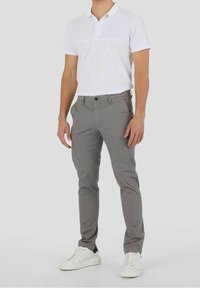 Chinos grises de corte slim, material de algodón, con bolsillos frontales y un cierre de un solo botón, combinados con una polo blanca y zapatillas blancas.