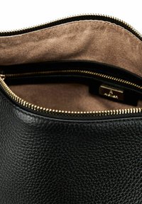 Intérieur de sac en cuir noir avec surface texturée. Comprend une fermeture éclair dorée et une doublure en daim lisse de teinte plus claire, mettant en avant un design minimaliste.