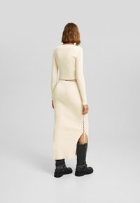 Ribbade stickade tvådelade set i creme, bestående av en kortärmad topp med långa ärmar och en midislång kjol med sidodelning och snörningsdetalj, matchat med svarta stövlar.