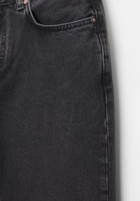 Gros plan sur un jean en denim noir montrant la poche avant, la boucle de ceinture et les rivets métalliques sur un tissu texturé.