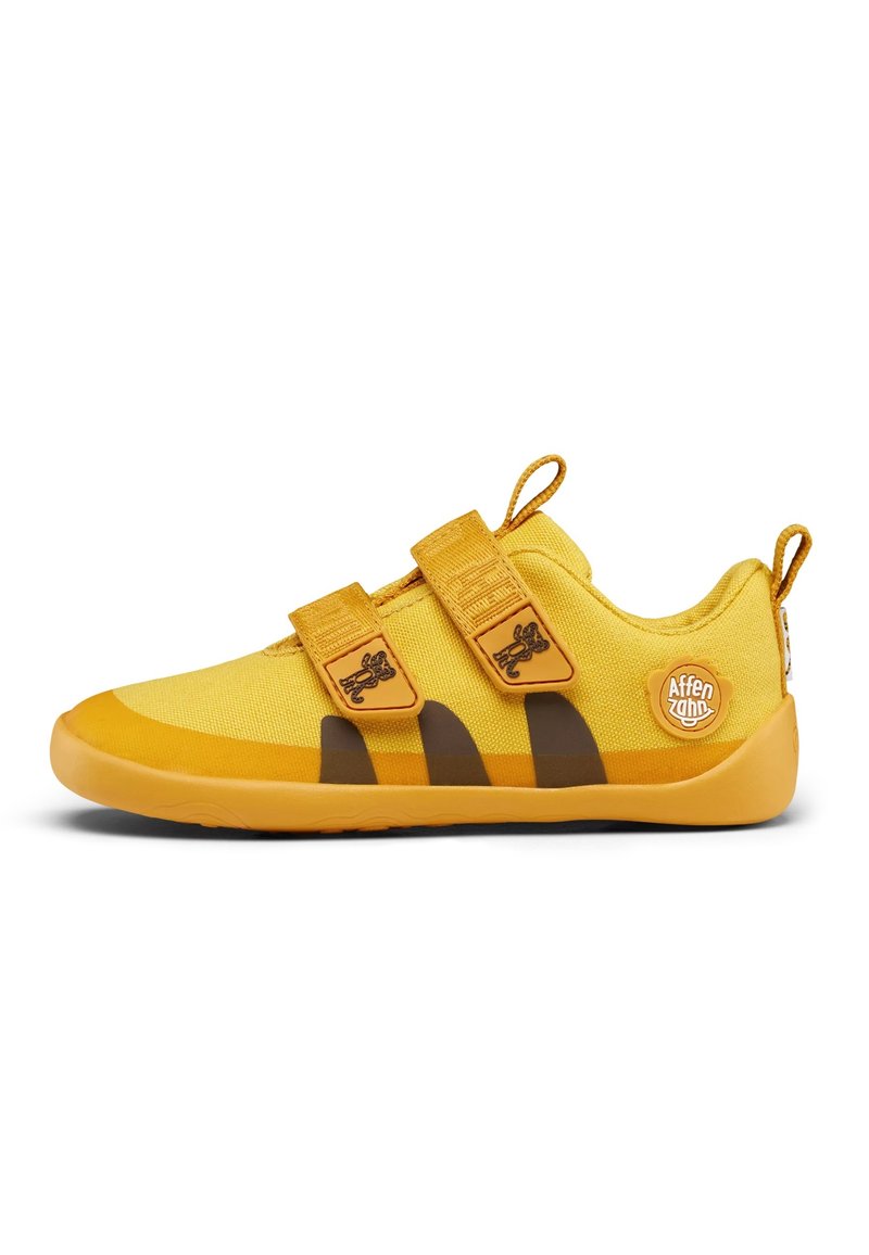 Gele stoffen sneaker met bruine gestreepte accenten, dubbele klittenbandriemen en rubberen zool. Heeft een ronde logo aan de buitenzijde.