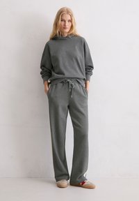 Szara bluza z kapturem z regulowanym sznurkiem, w połączeniu z pasującymi spodniami ze sznurkiem z bocznym akcentem. Miękki, wygodny materiał o luźnym kroju.
