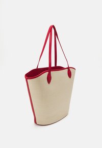 Tote-väska gjord av texturerat beige material med accentfärger i röd syntetisk läder. Har två röda handtag och en rymlig öppen topp.