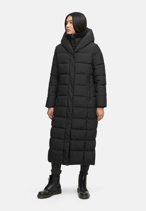 Sort lang dunjakke med hætte, med et quiltet design, lynlås lukning og sidelommer. Båret over sorte bukser og støvler.