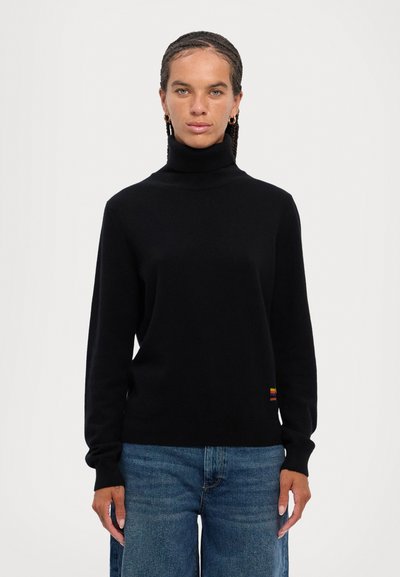 Black turtleneck sweater with long sleeves, made of textured fabric. Features a multicolored stripe near the hem. Paired with blue denim pants.