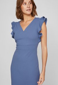 Blue fitted dress with a V-neck, ruffled cap sleeves, and smooth textured fabric. Emphasizes a structured silhouette.