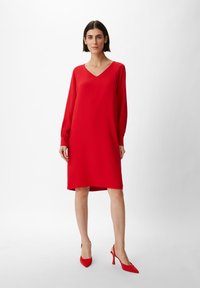 Rotes langärmliges Kleid mit V-Ausschnitt, lockerem Schnitt und glattem Stoff. Kombiniert mit passenden roten spitzen High Heels.