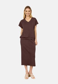 Top marrone con scollo a V e maniche corte abbinato a una gonna midi coordinata. Tessuto liscio con vestibilità rilassata. Indossato con sandali con cinturino.