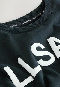 Must mustikas, mille esiküljel on julge valge tekst "ALLSAINTS". Ribbiga krae ja äär, pehme tekstuur, minimalistik disain.