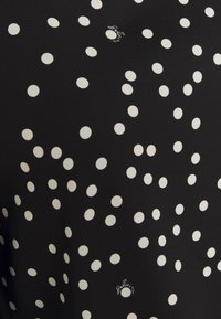 Tissu noir avec un motif irrégulier de pois blancs et de petits textes en écriture cursive dispersés entre les pois.